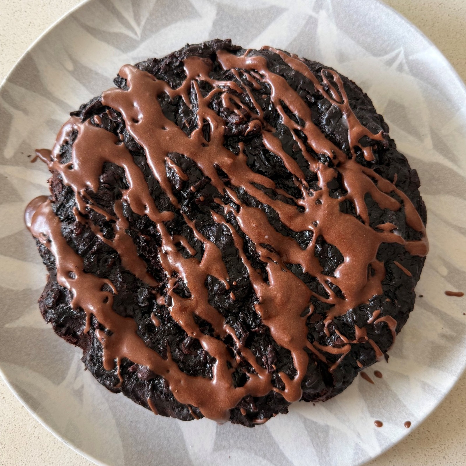 Fudgy chocolate beetroot cake drizzled with chocolate icing on a patterned plate
