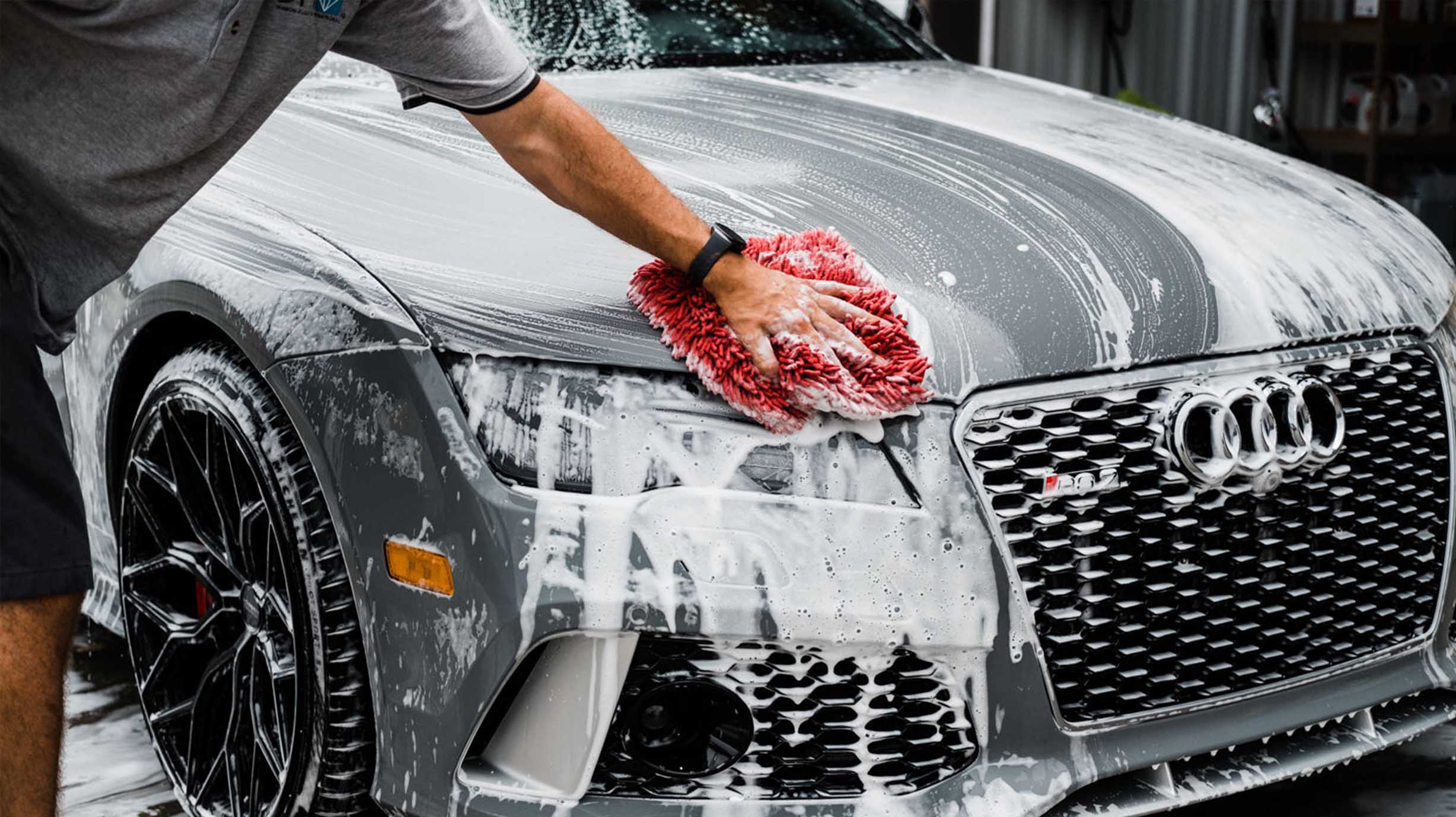 Detailer hand washing a gray Audi with a soapy red wash mitt