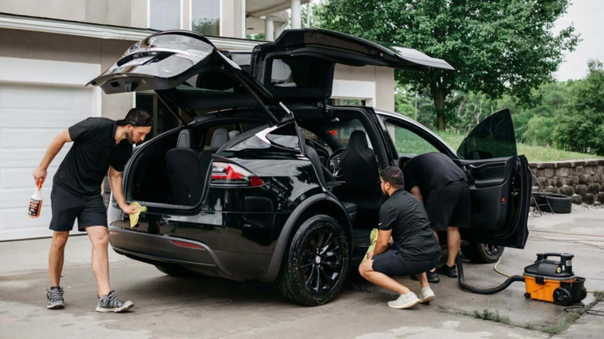 Three detailers cleaning a black Tesla Model X in a driveway