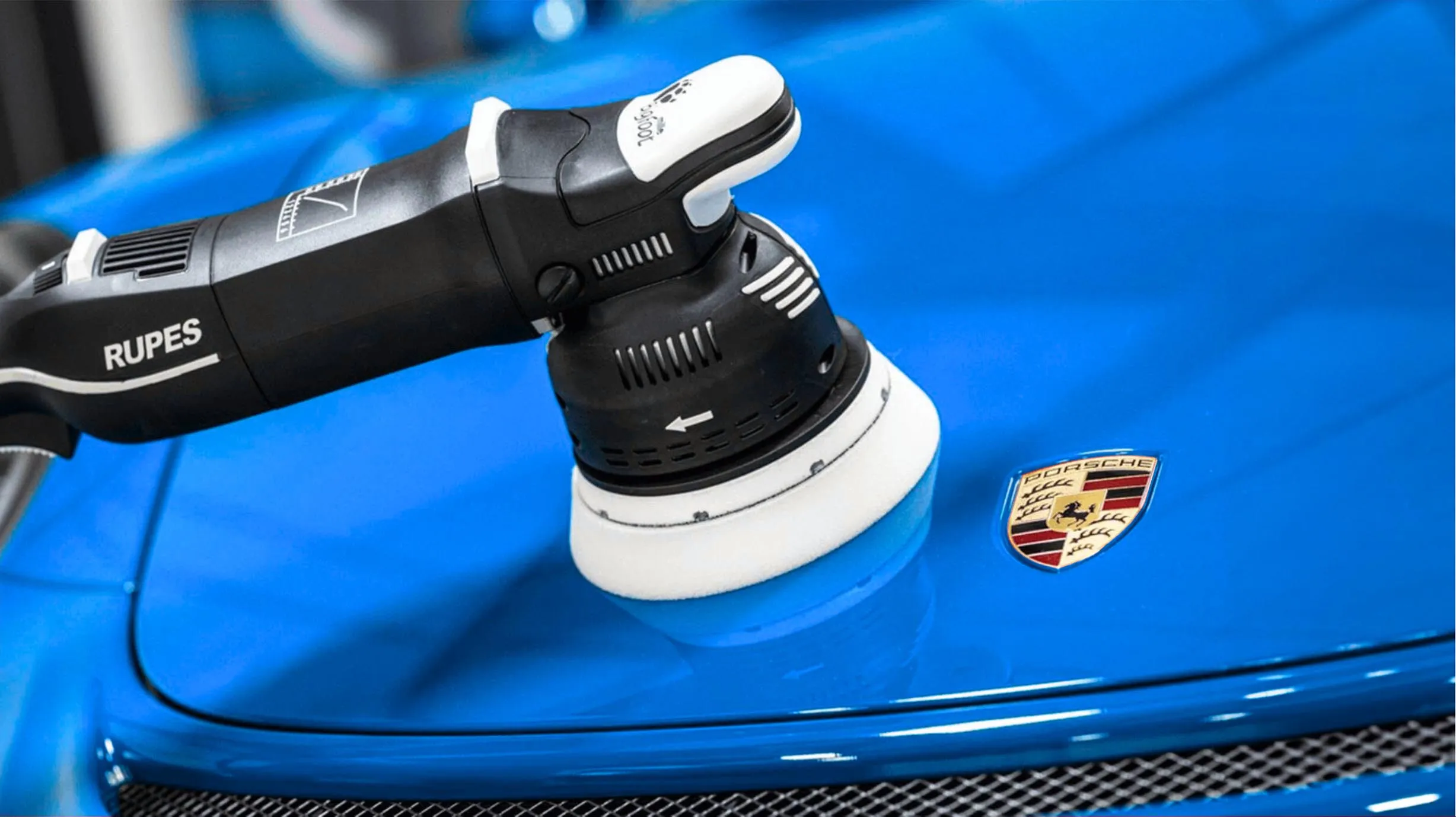 Dual action polisher on the hood of a blue Porsche