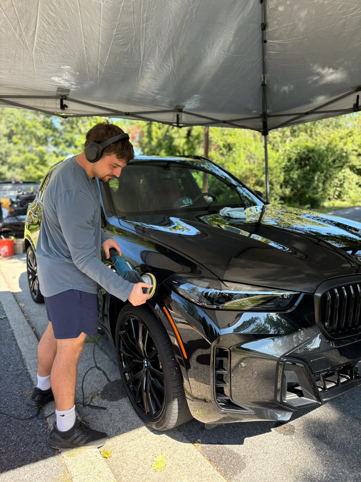 KBC Auto Detailing technician machine polishing a black BMW SUV under a canopy