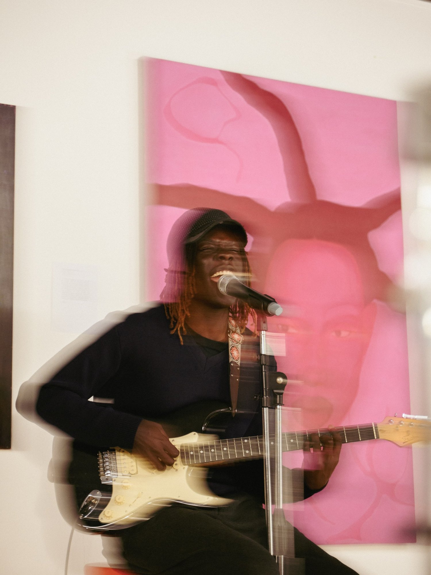 A guitarist plays a live set against a pink artwork