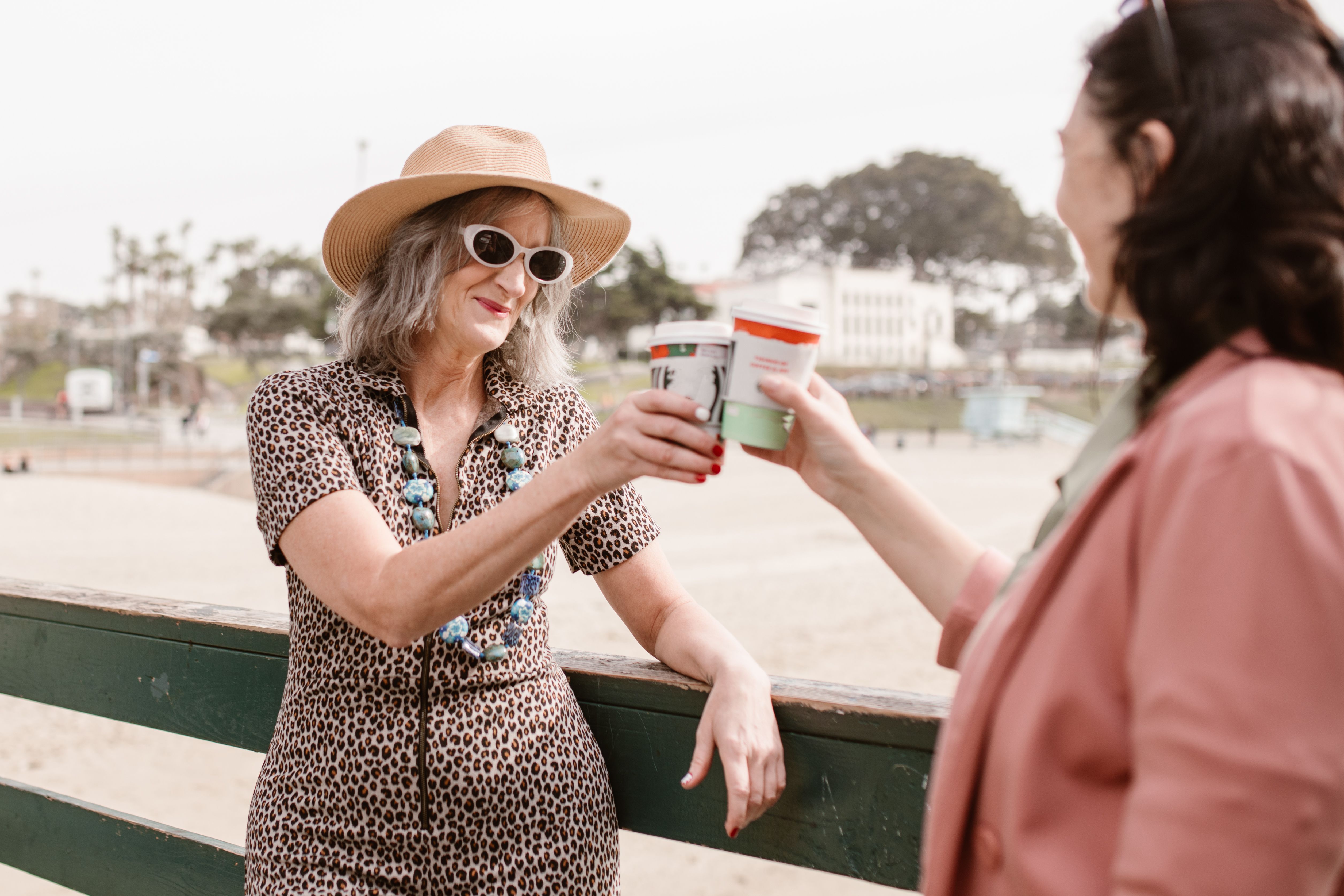 Two women laughing and toasting with drinks by the beach