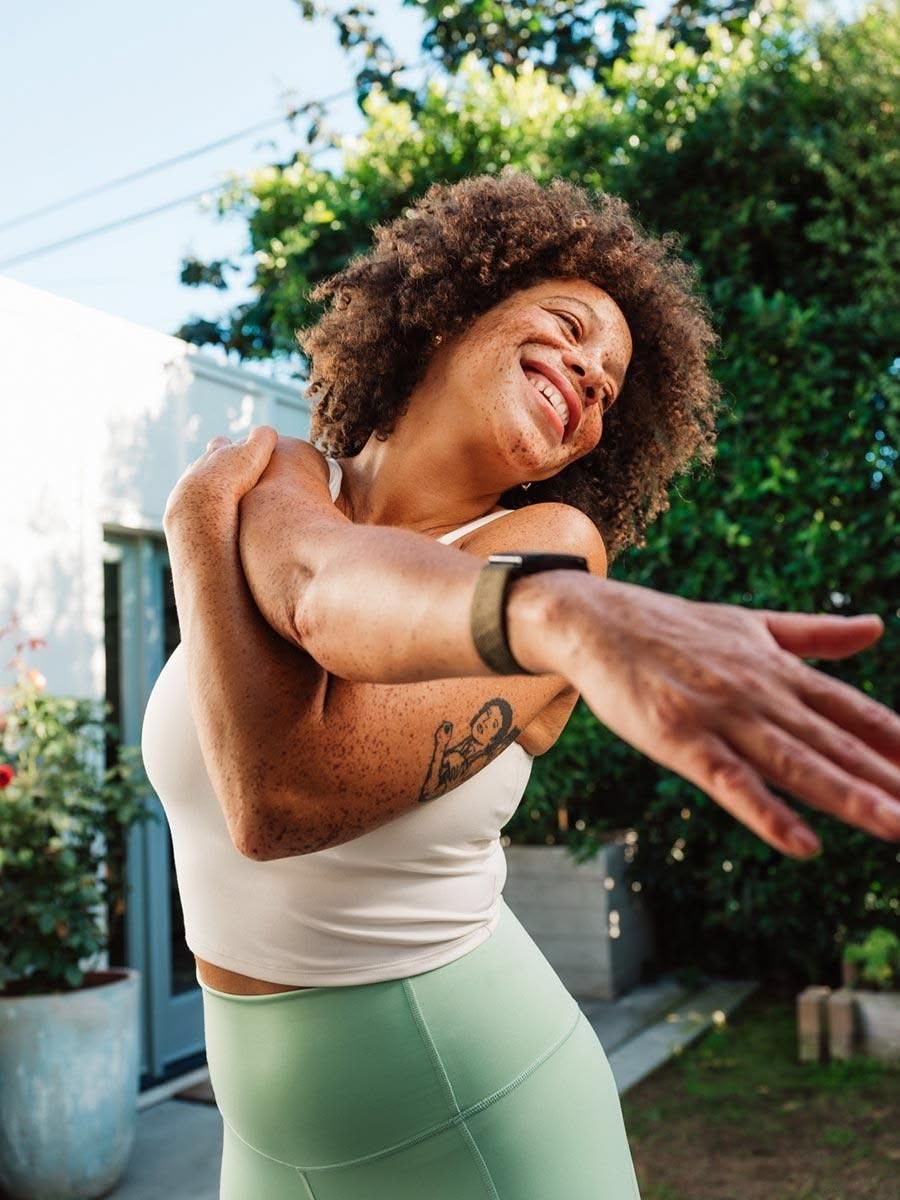 A smiling woman stretching outdoors in her garden