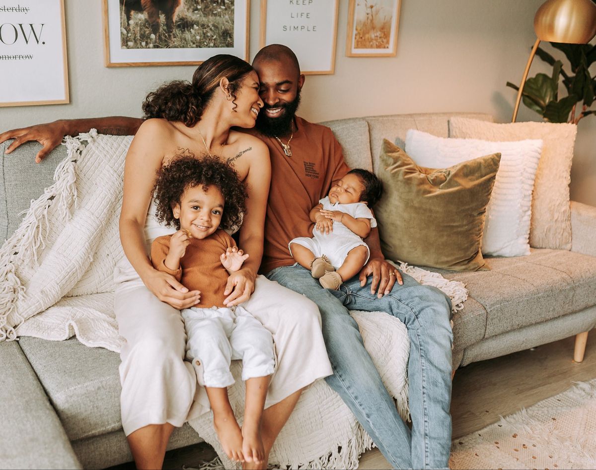 A smiling family with two young children relaxing together on a sofa at home