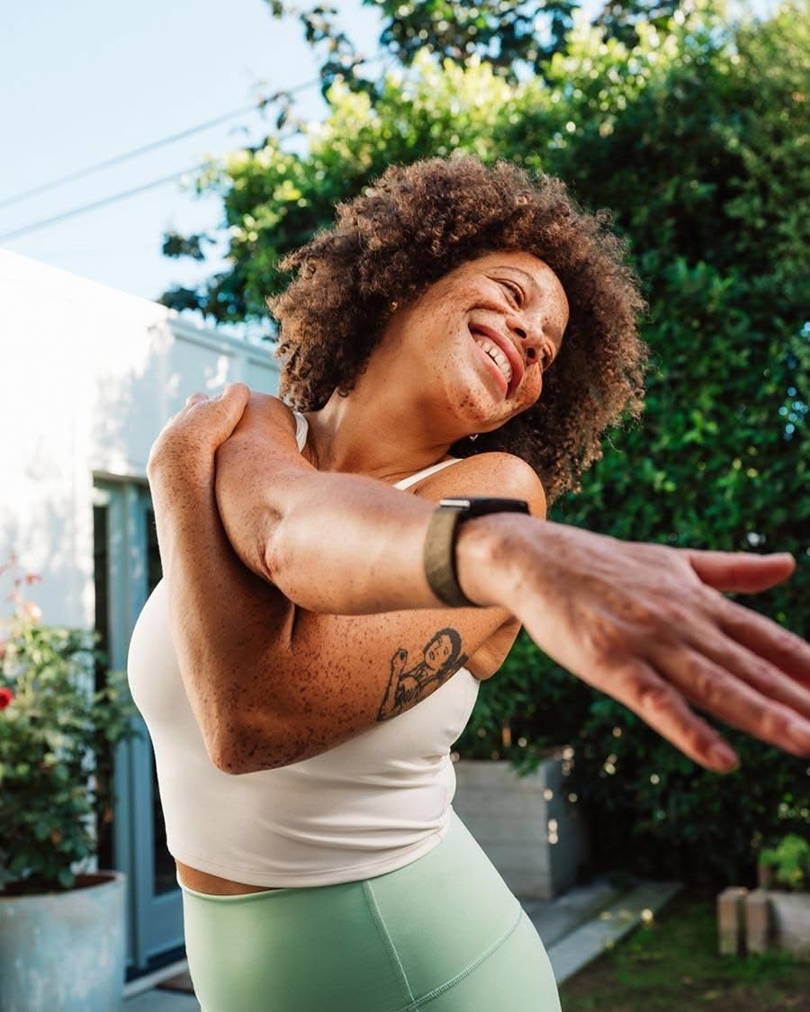 A woman laughing as she stretches outdoors