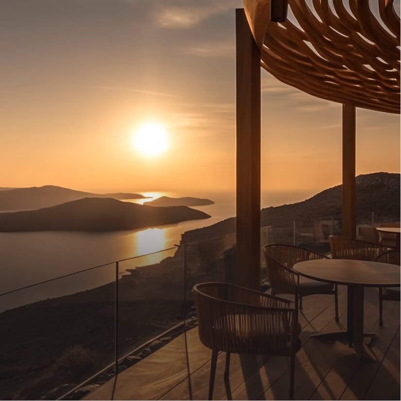 Sunset over a calm sea with multiple islands, viewed from a terrace with wooden furniture and a woven pergola casting shadows.