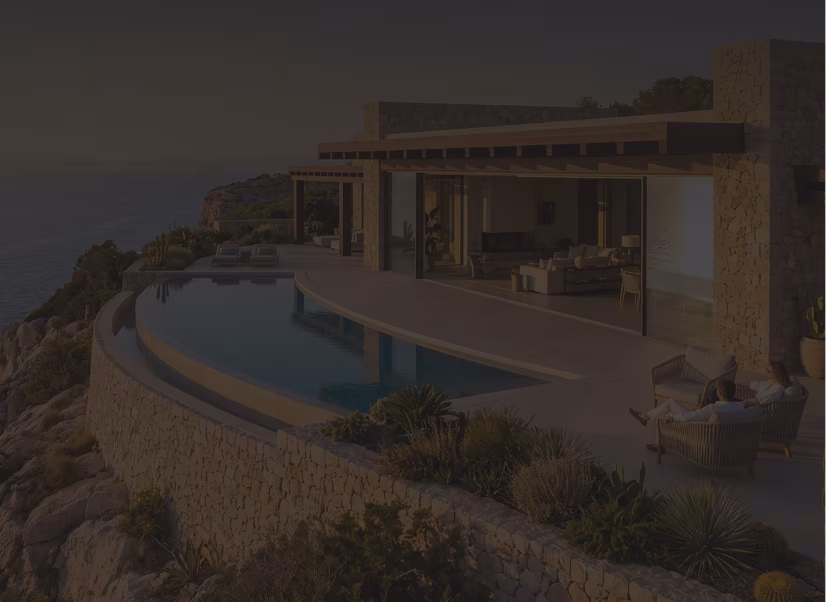 Modern stone and glass house with an infinity pool overlooking a rocky coastline with ocean view during sunset, with lounge chairs and outdoor seating on the terrace.