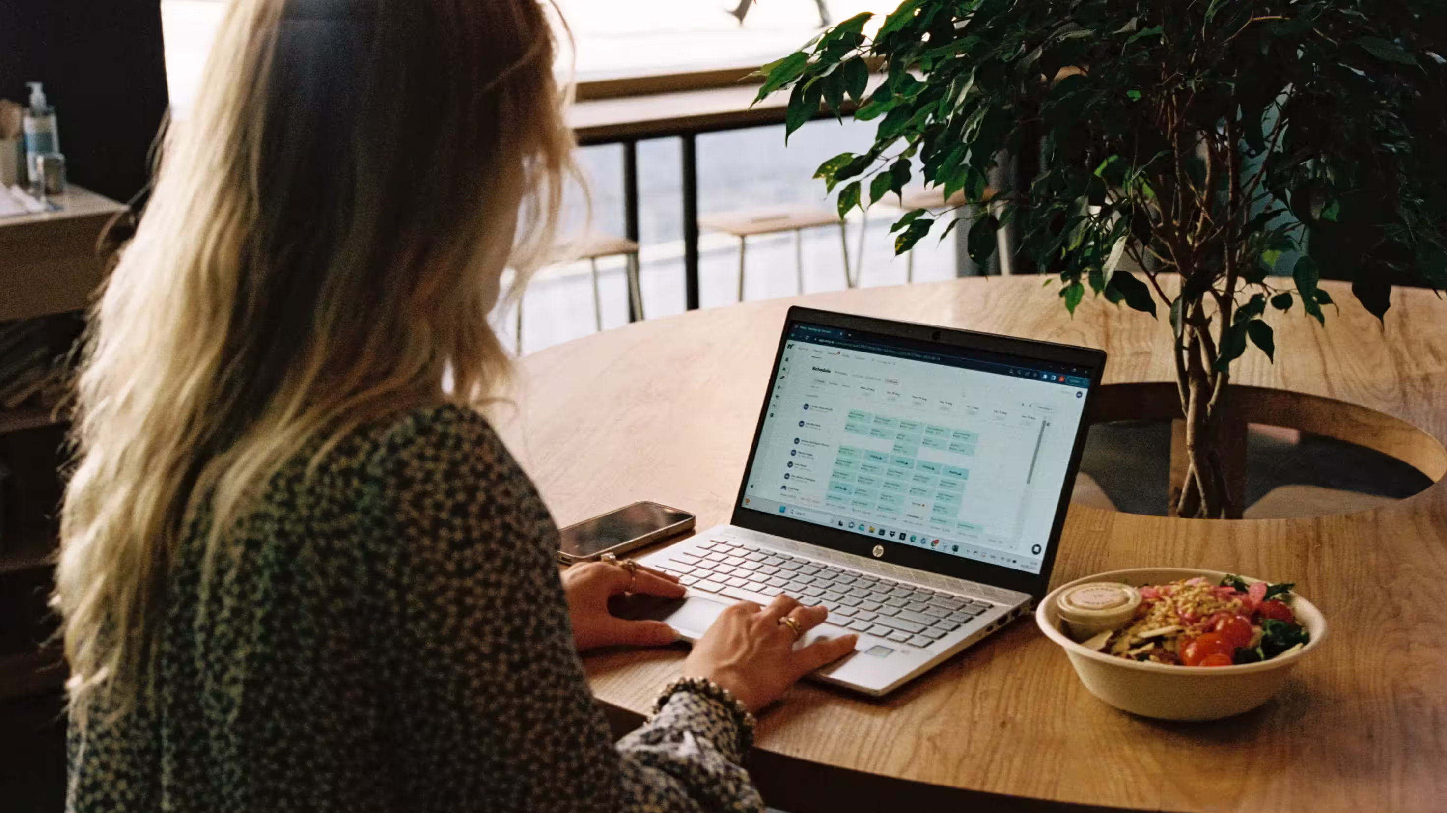 Woman using a laptop in a cafe with a salad bowl and phone nearby