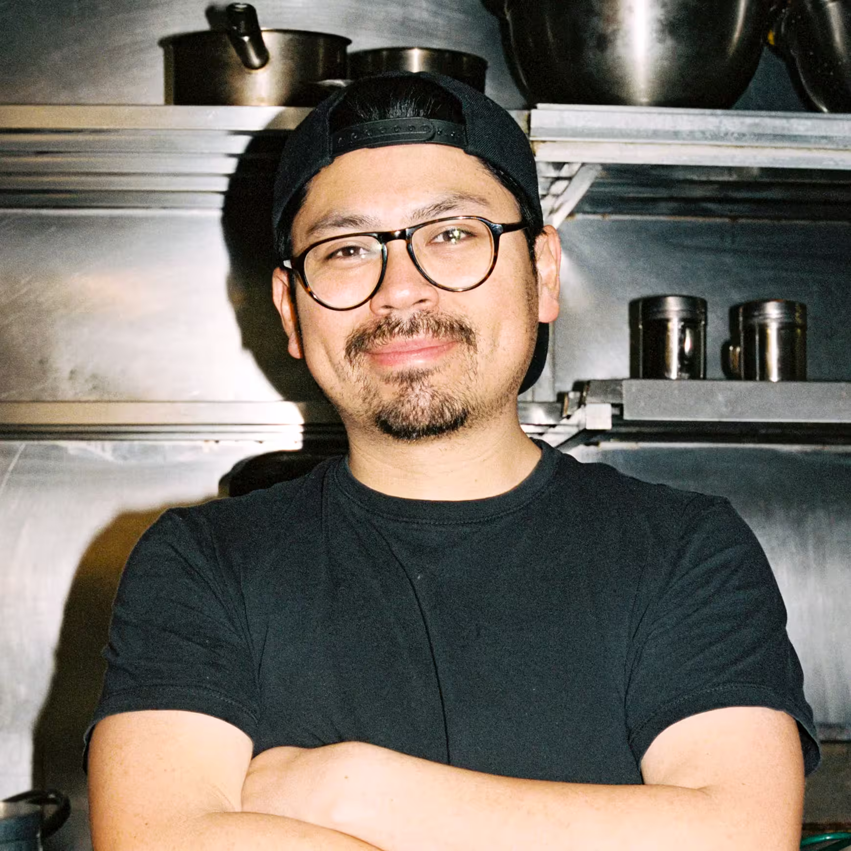 Chef in black t-shirt and glasses smiling in a commercial kitchen