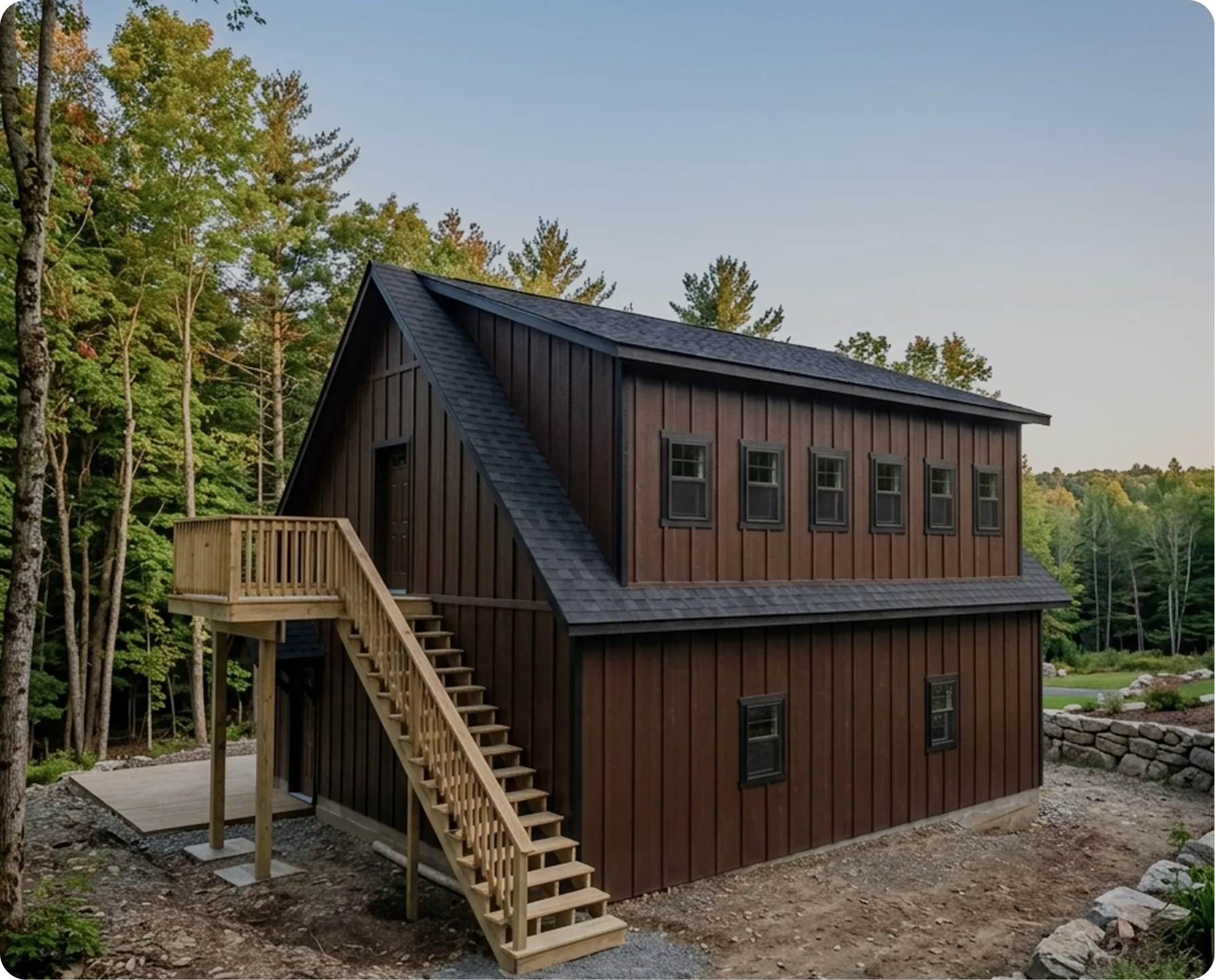A dark brown two-story barn-style building with an external wooden staircase leading to a second-floor deck.