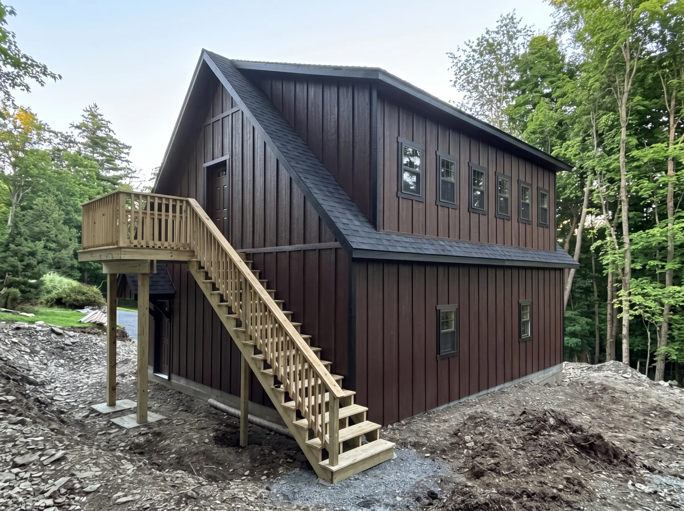 Two-story dark brown barn-style building with a wooden exterior staircase leading to a second-floor deck.