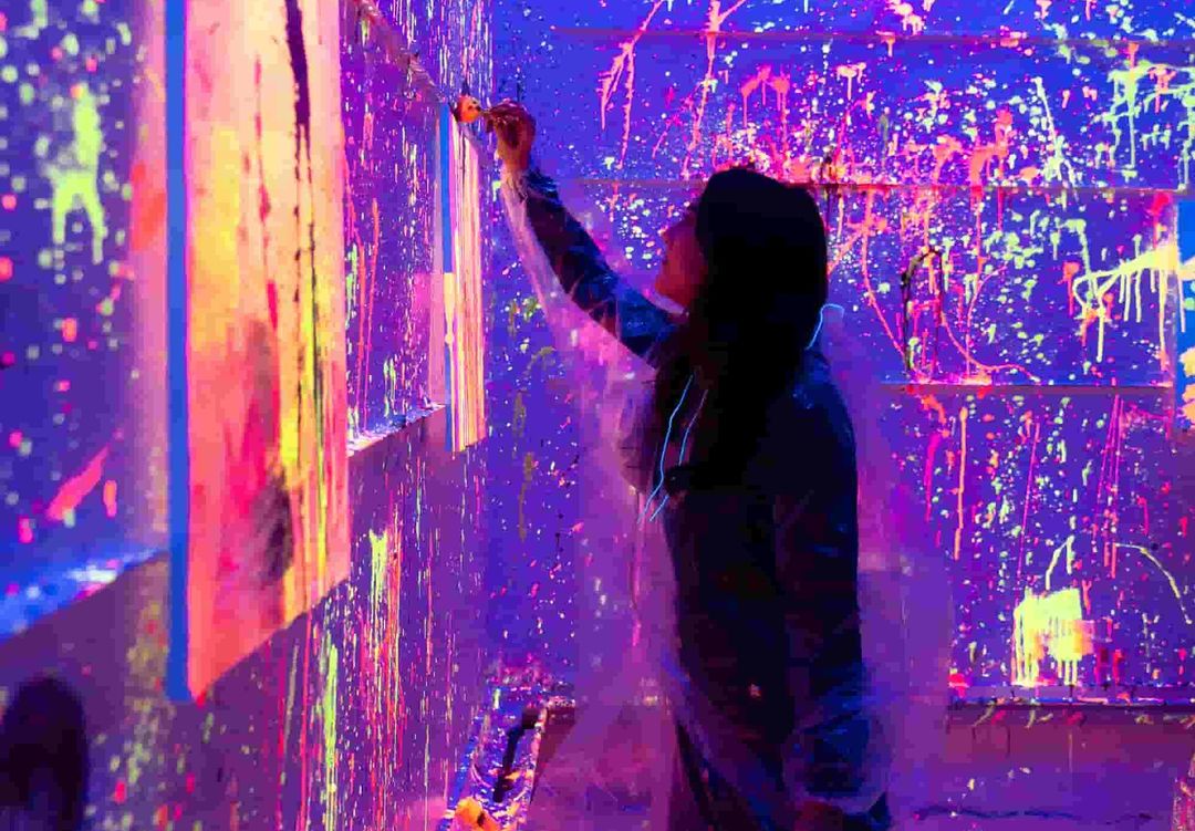 Femme qui peint une toile en peinture fluo sous lumière noire chez Paint Invaders Paris