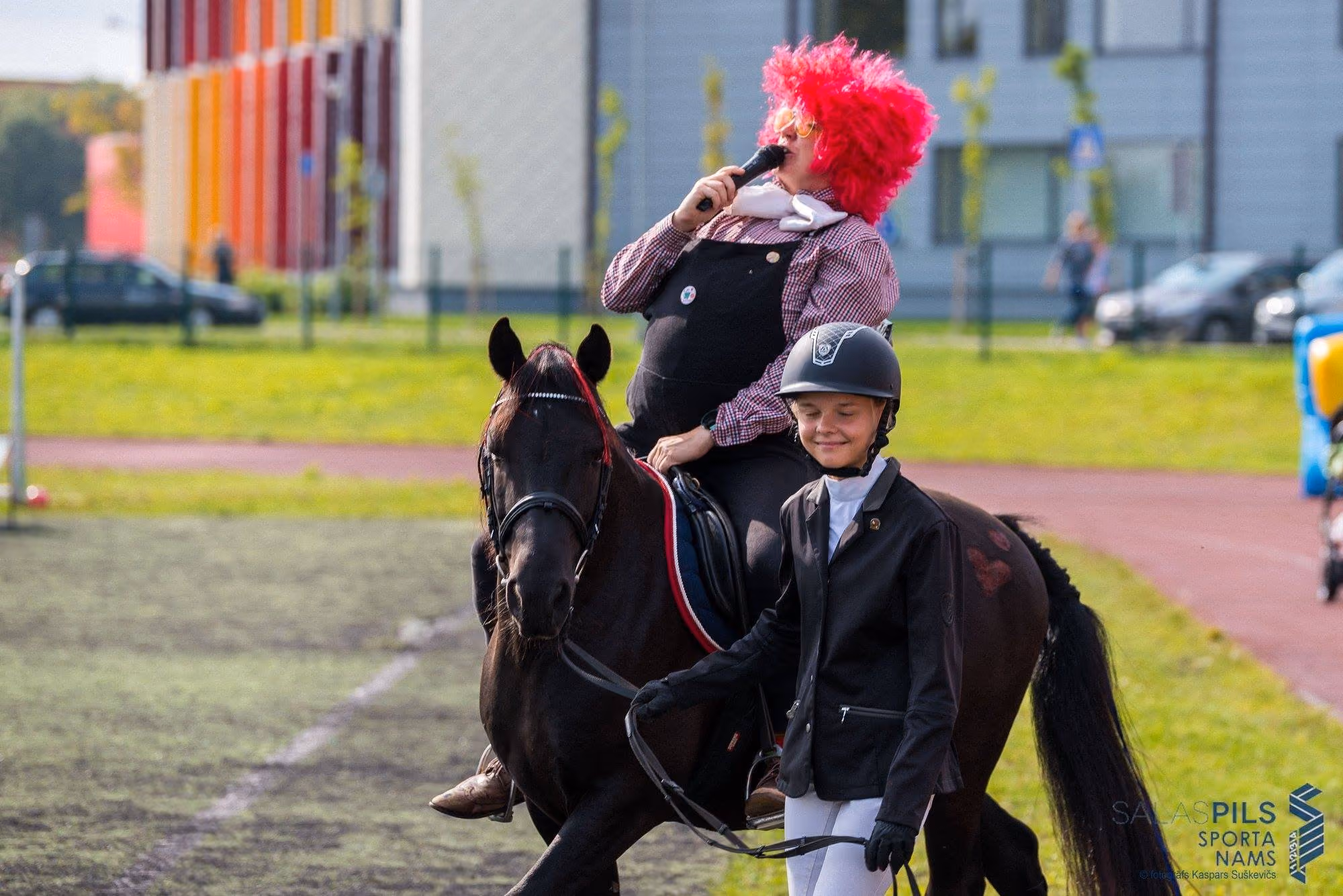 Klauns ar mikrofonu un bērns uz ponija sporta svētkos