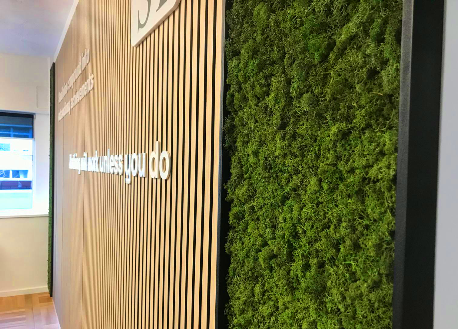 Office installation combining vertical timber slats, dimensional lettering and preserved moss