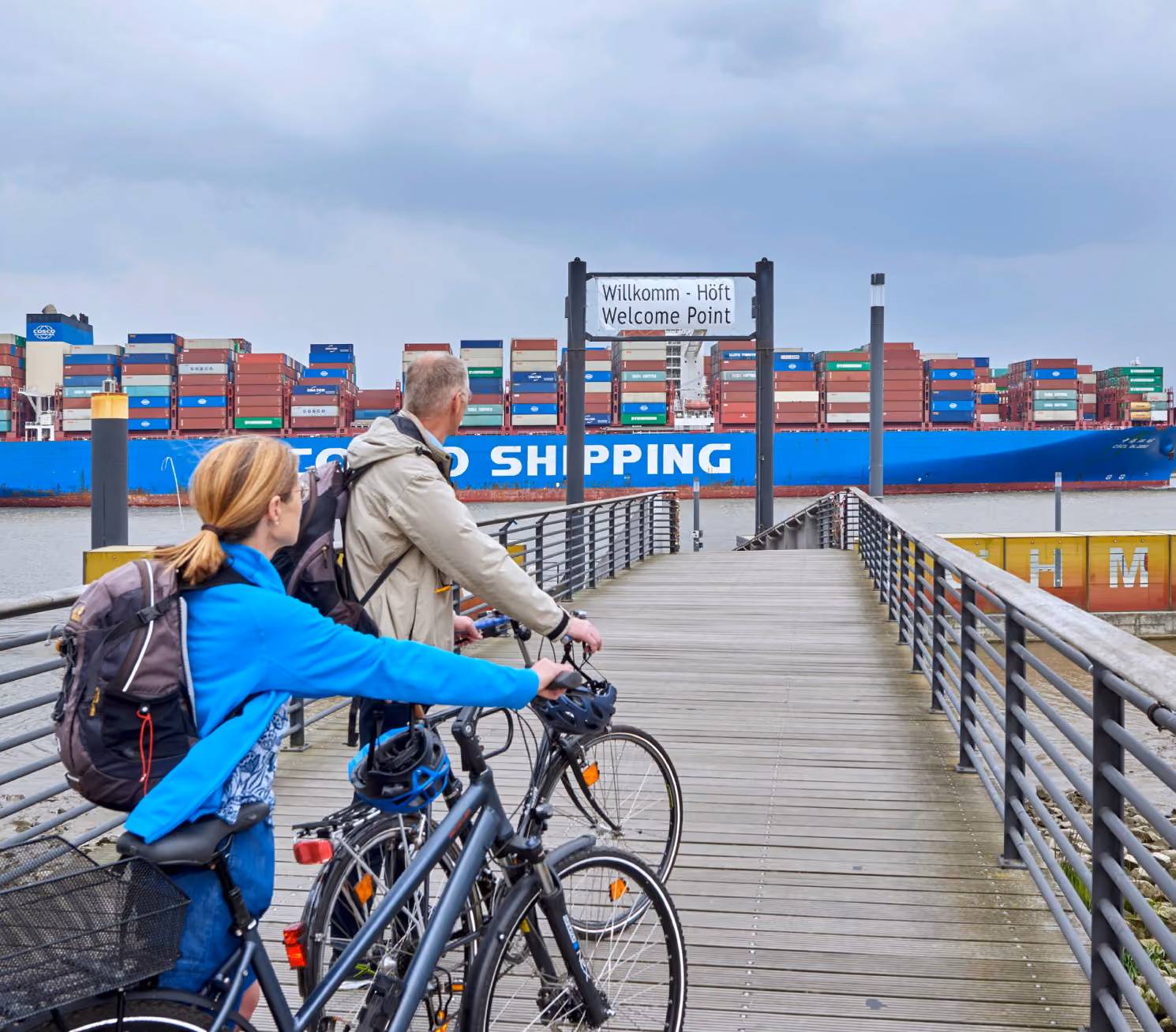 Radreisende am Nord-Ostsee-Kanal mit Blick auf ein Containerschiff
