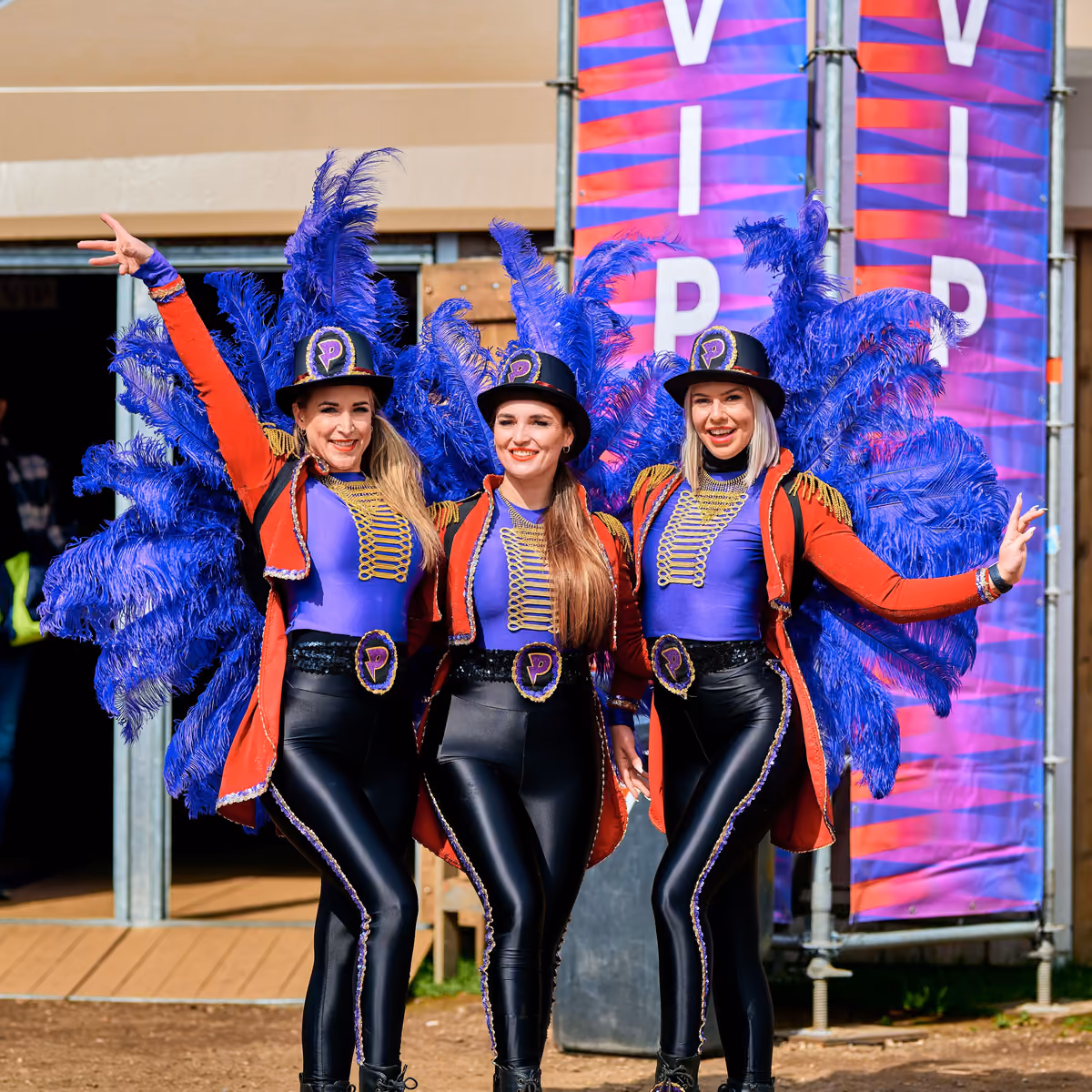 Drie hostessen in circuskostuum met blauwe veren bij de VIP-ingang