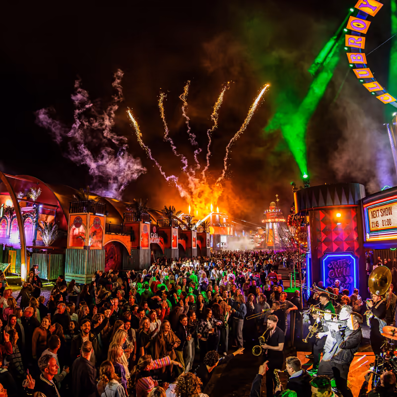 Vuurwerk en groene lasers boven een druk festivalplein, met een fanfare tussen het publiek