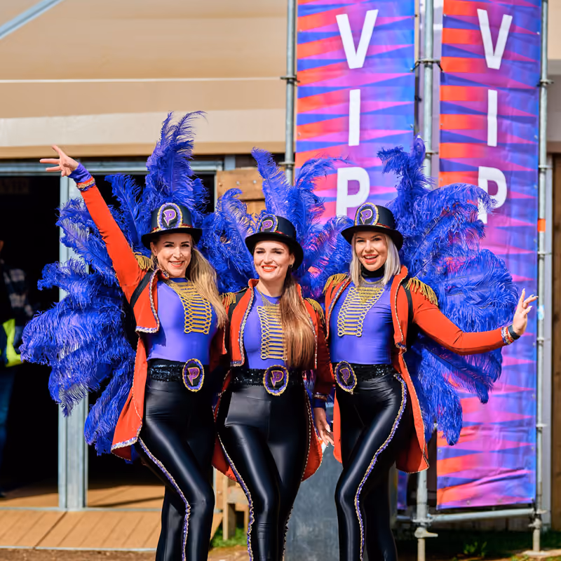 Drie hostessen in circuskostuum met blauwe veren voor de VIP-banners