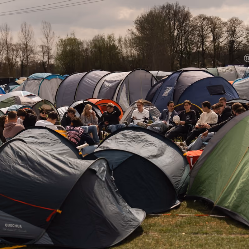 Een groep vrienden zit samen in het gras tussen hun tenten in de Vriendenarea