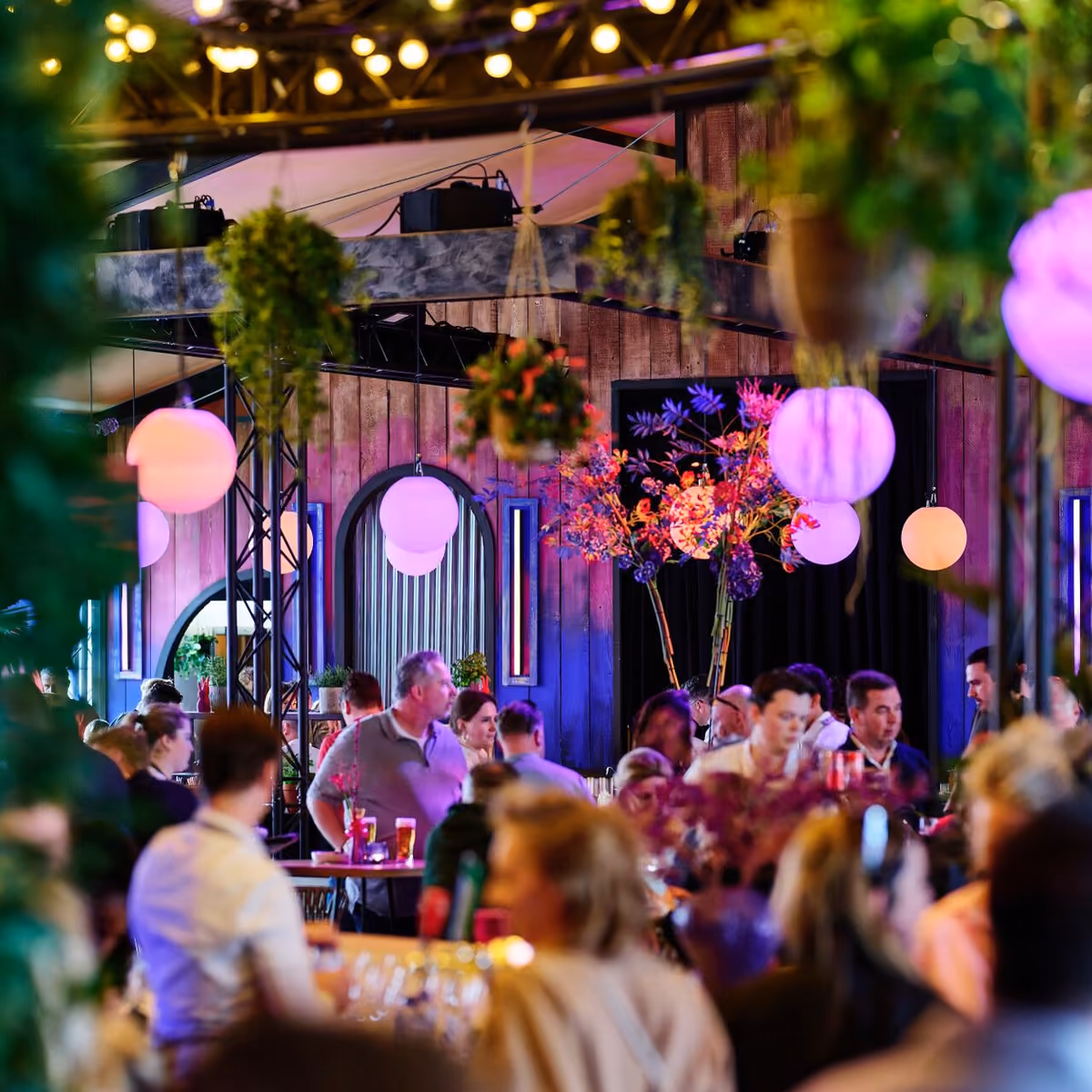 Gasten aan tafel in de VIP Lounge onder roze lampionnen, bloemen en hangende planten