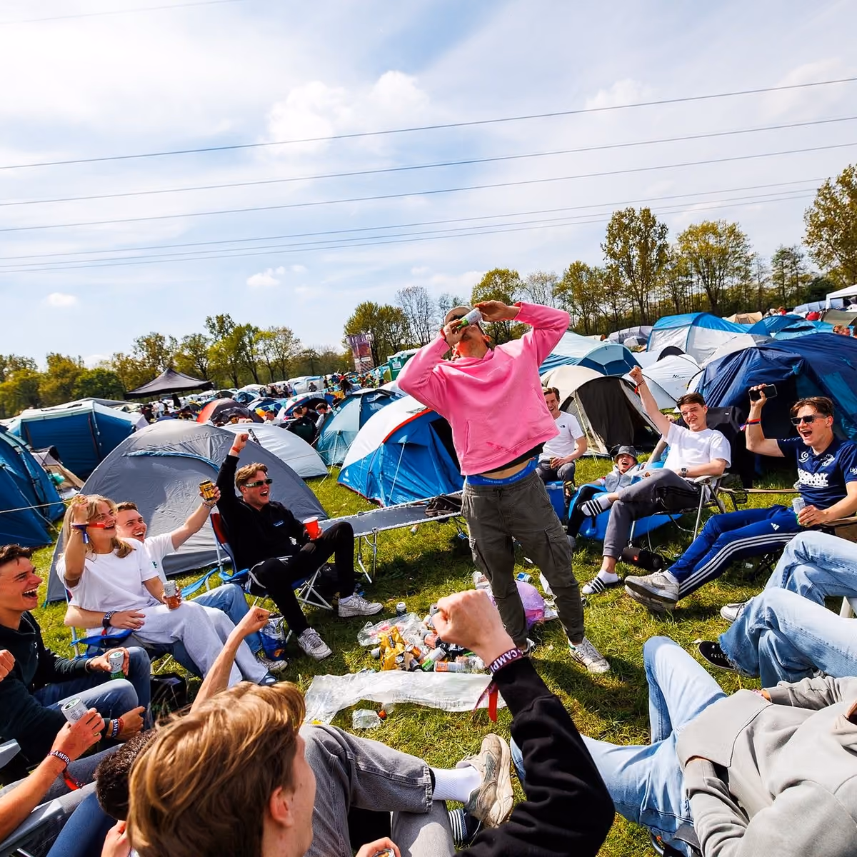 Een groep vrienden ligt en zit in het gras tussen de tenten van de Vriendenarea