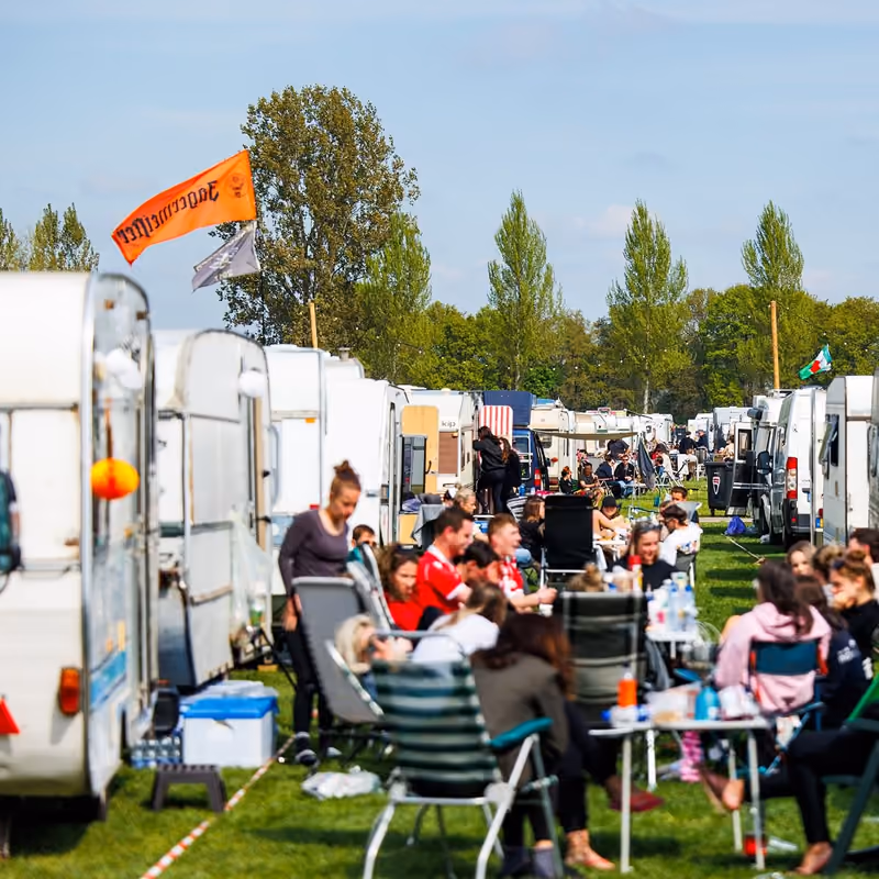 Kampeerders zitten in tuinstoelen voor een lange rij caravans op Paradise City