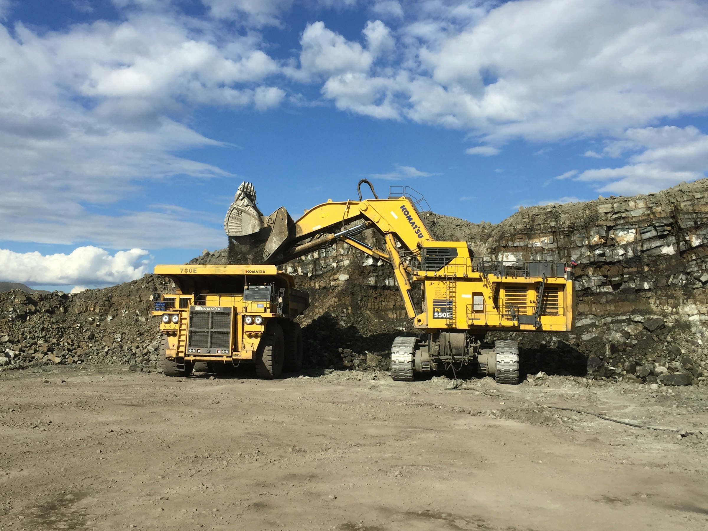 Stor gravemaskin som laster stein på en gul dumper