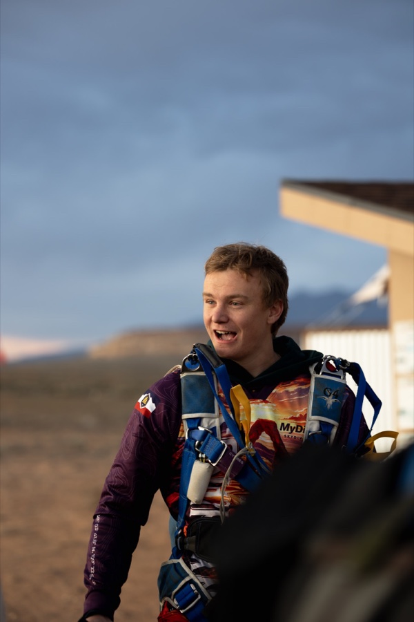 A jumper in a rig grinning on the ground at dusk