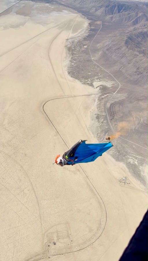 A wingsuit flyer over open desert, seen from the aircraft