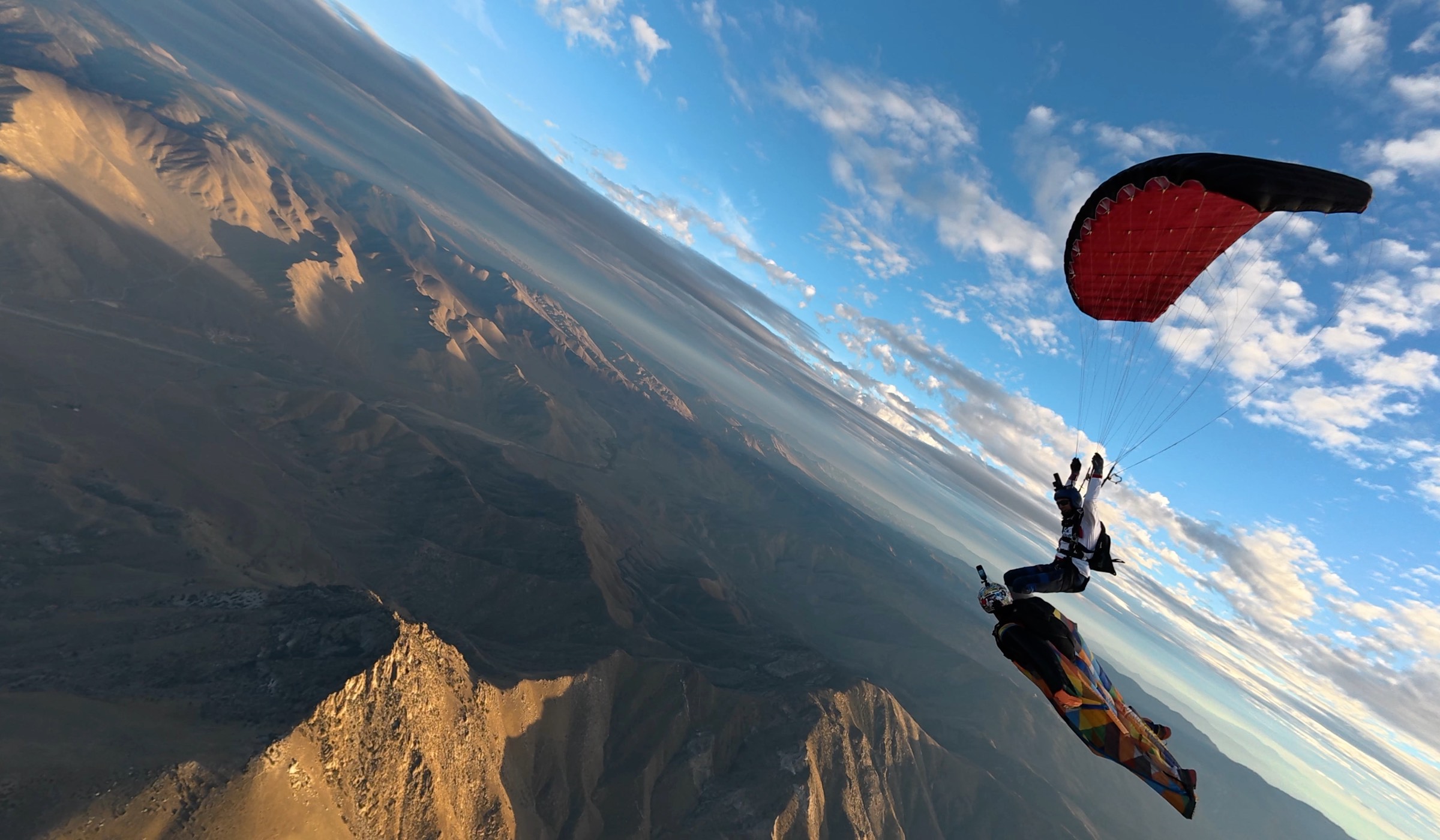 A wingsuit flyer and a canopy over a mountain ridge at golden hour