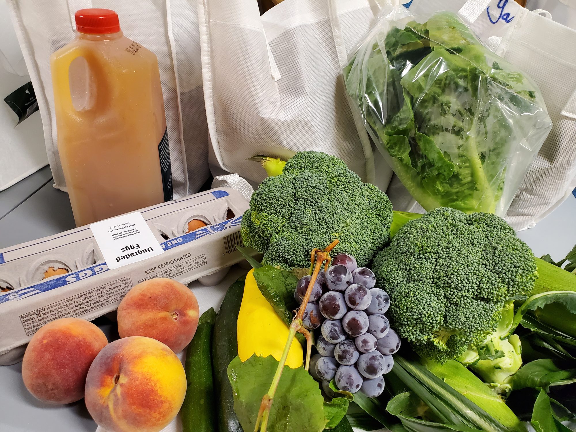 A Milk Lady CSA share of broccoli, peaches, grapes, squash, lettuce, a dozen eggs and a jug of cider