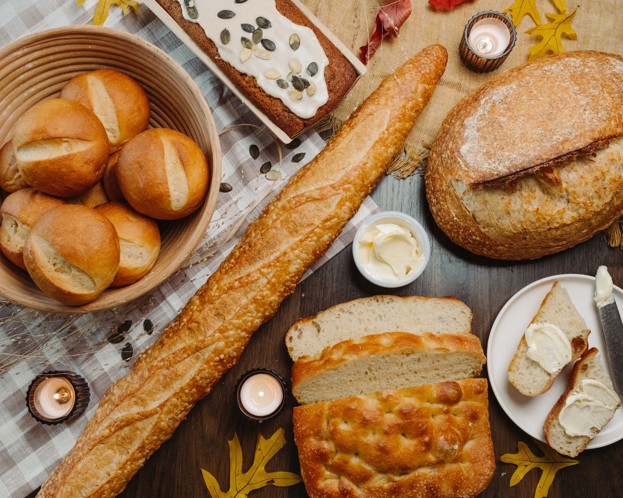 A styled spread of baguette, dinner rolls, a sourdough loaf, focaccia and sliced bread with butter
