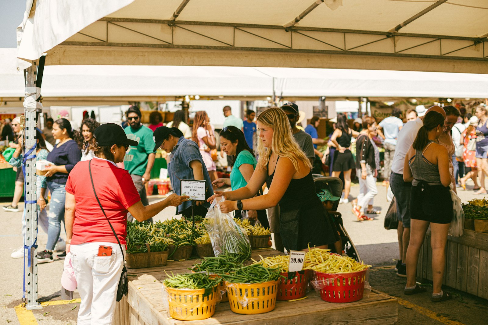 Shoppers browsing produce under tents at an outdoor market