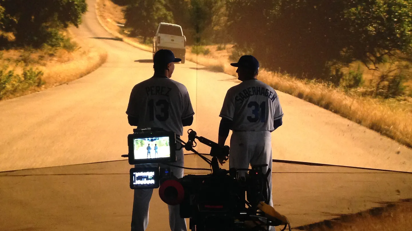 Salvador Perez and Bret Saberhagen on set in front of a projected country road, camera rig in the foreground