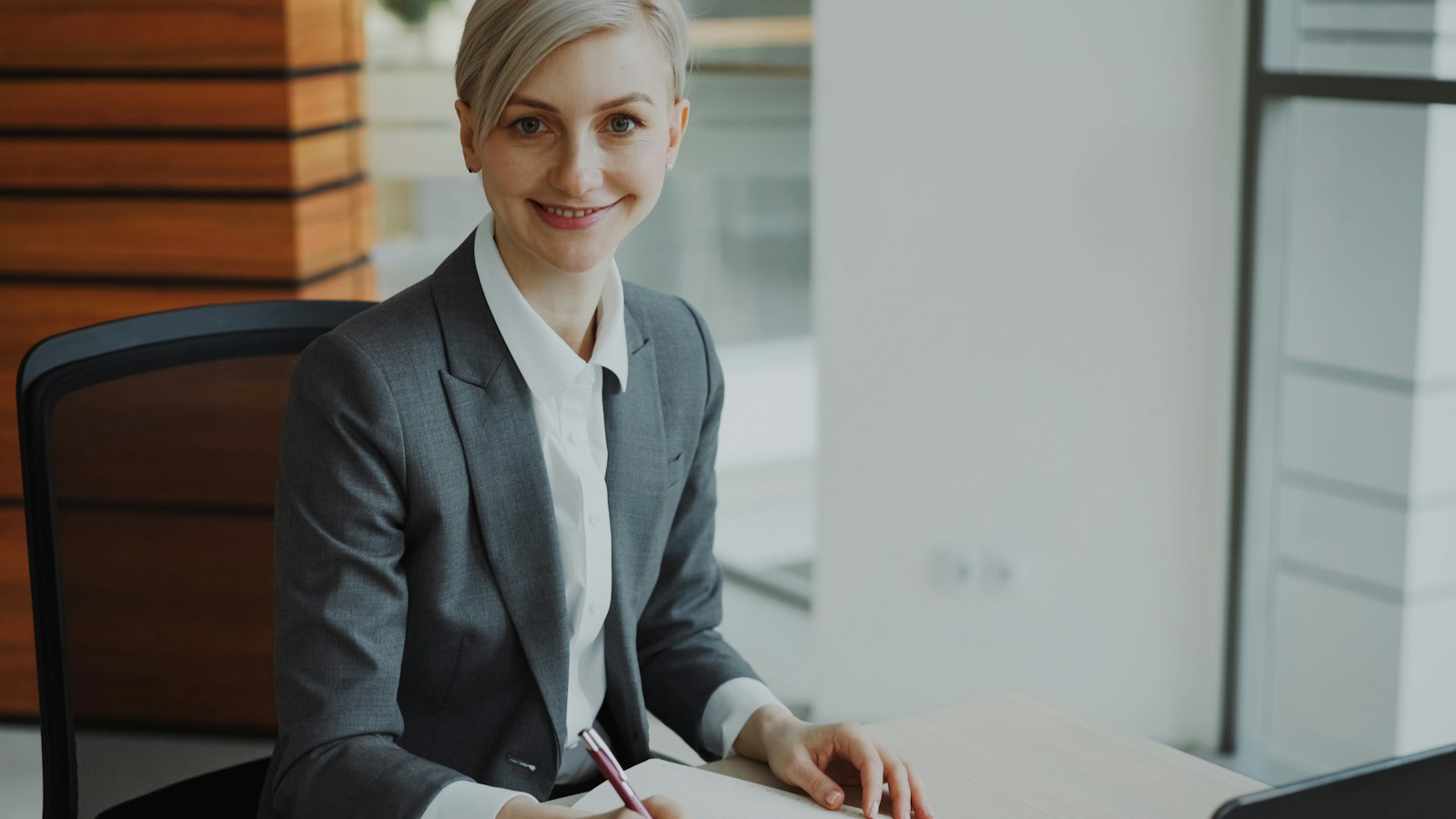 Smiling compliance lead making notes at her desk