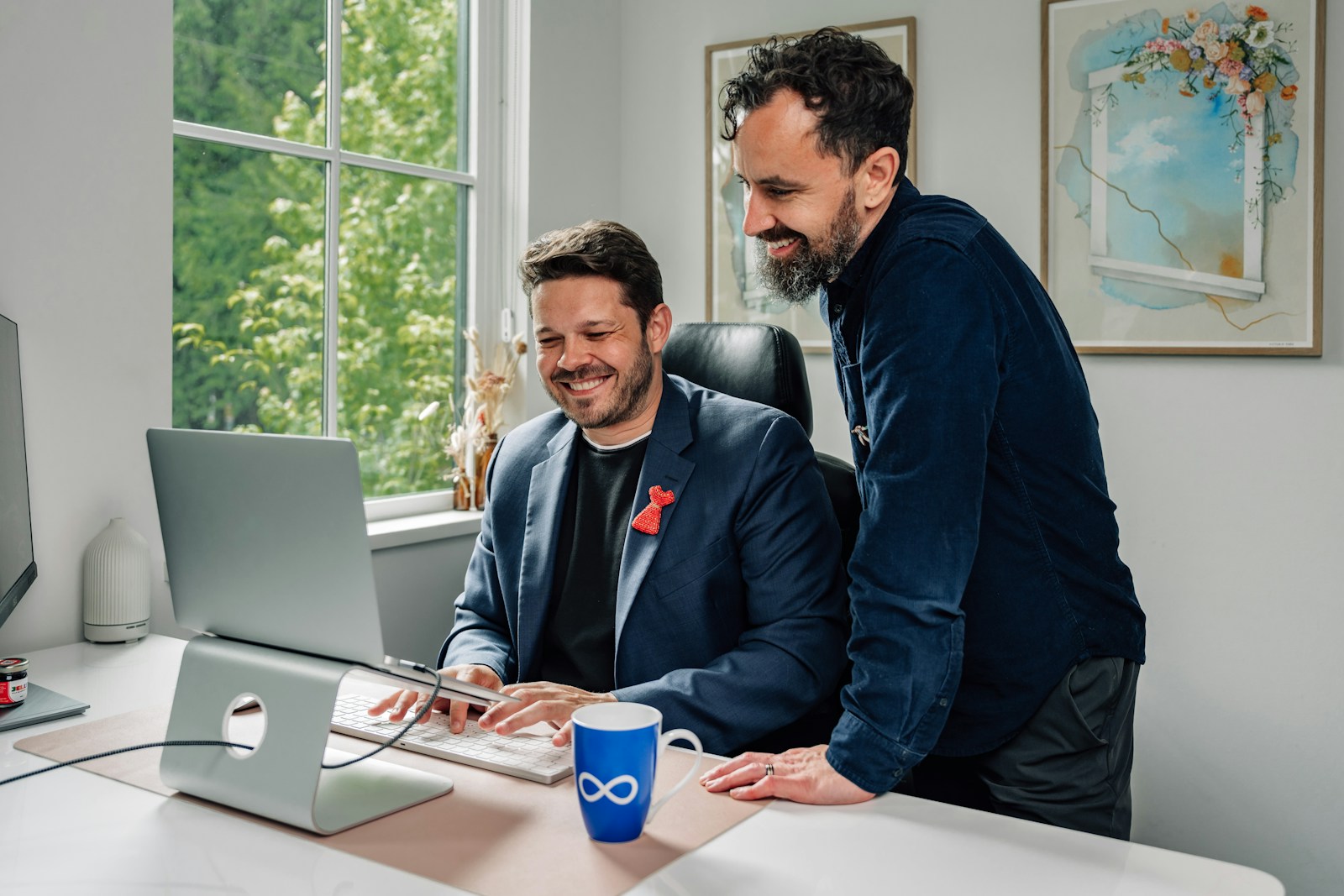Two colleagues smiling at a laptop in a bright office