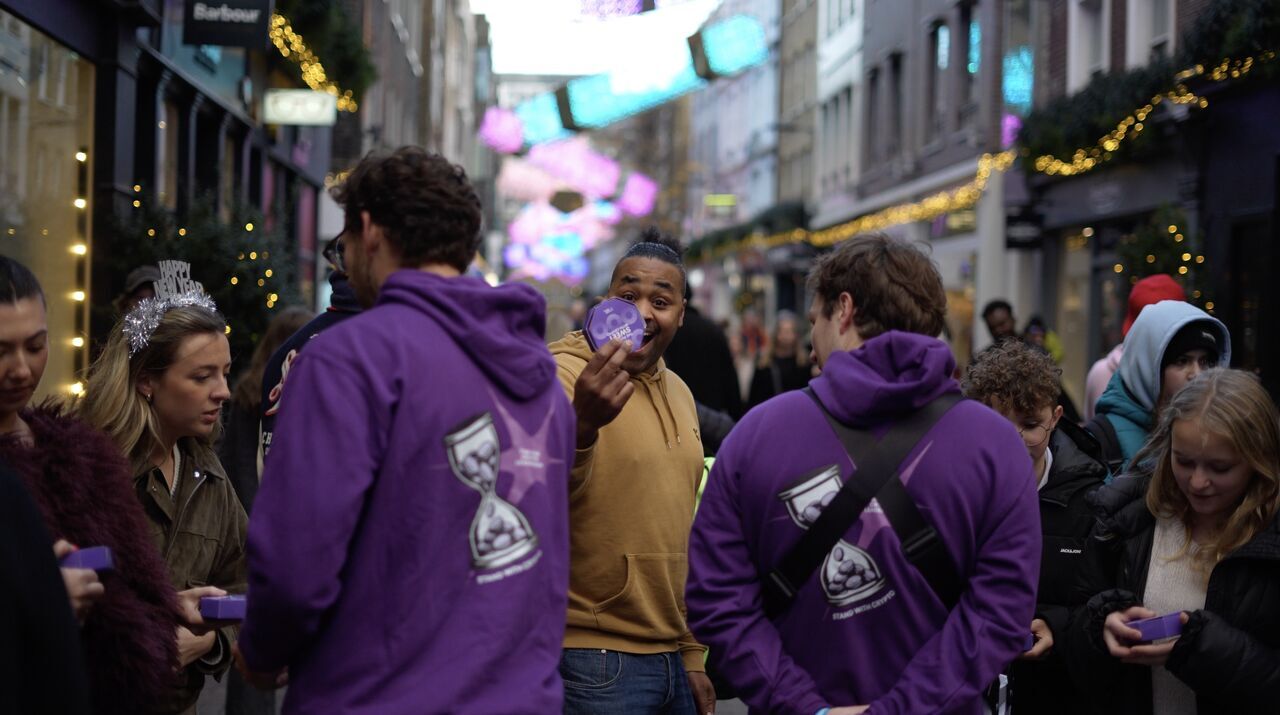 Stand With Crypto team in purple hoodies handing out donuts to shoppers on a London street