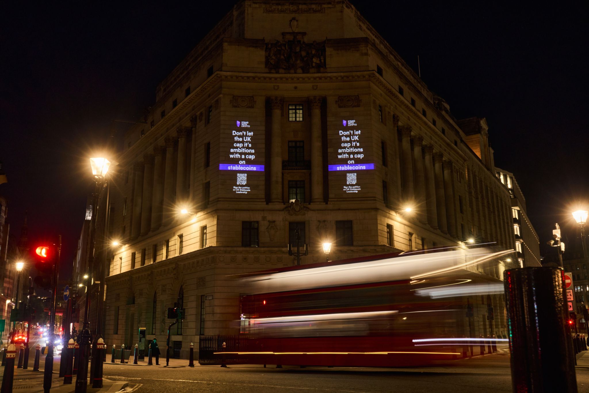 Stand With Crypto stablecoin message projected onto a London building at night as a red bus passes