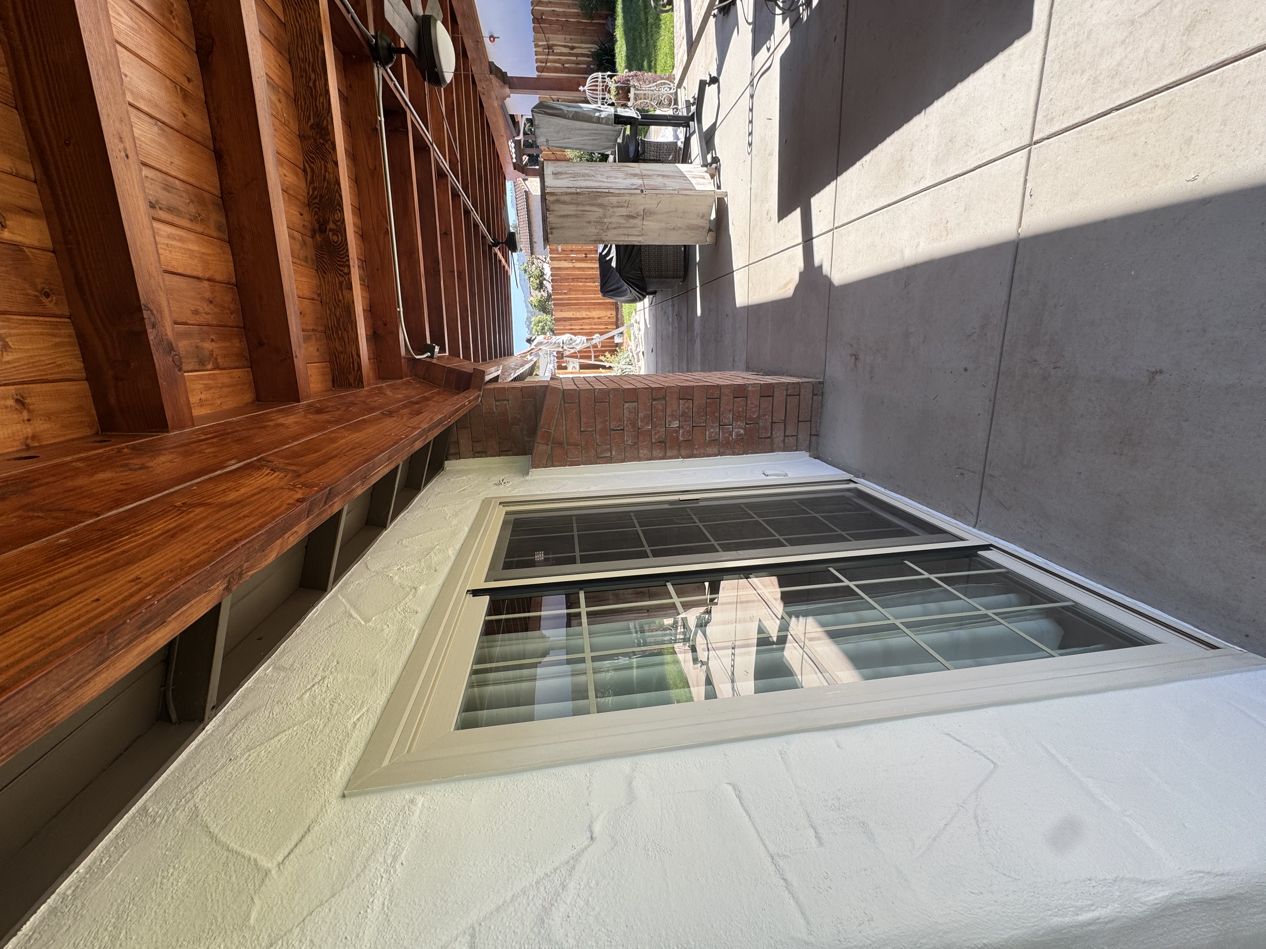Close view of white stucco exterior wall, window trim and timber patio cover
