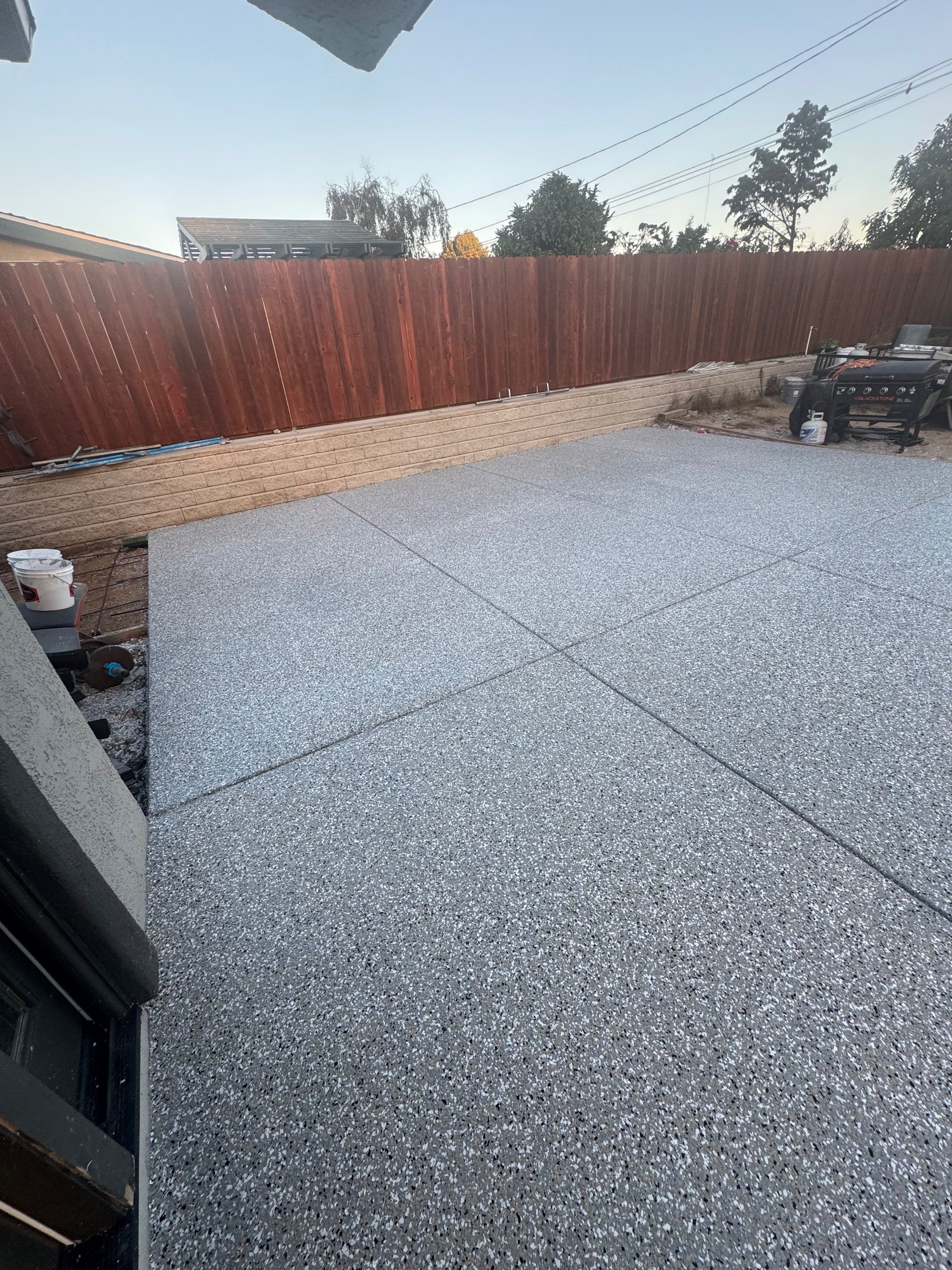Gray decorative flake coating on an outdoor concrete patio beside a redwood fence