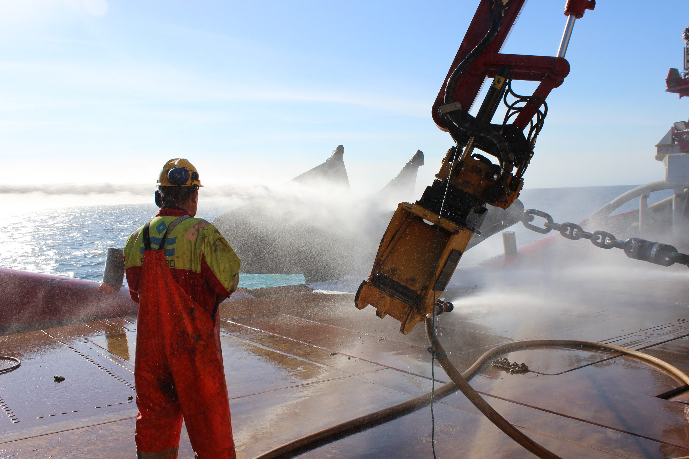 Deckhand washing down anchor chain on an anchor handling vessel