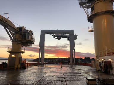 View of a ship's deck at sunset with large industrial cranes and equipment under a partly cloudy sky.