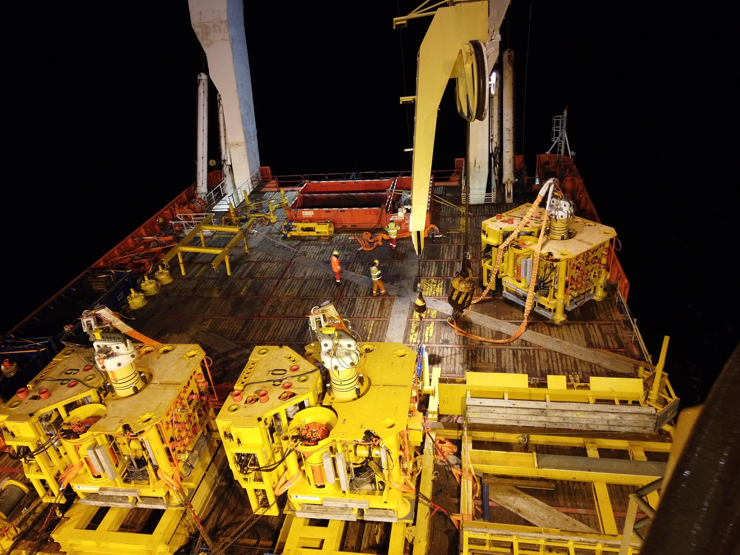 Wellhead tooling and subsea equipment on a vessel's deck at night