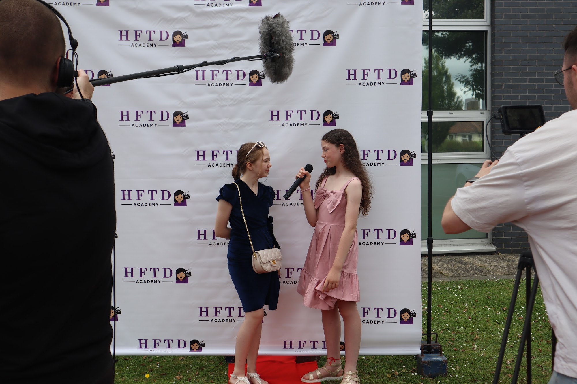 Two HFTD Juniors filming a scene in front of the HFTD Academy backdrop with a boom mic