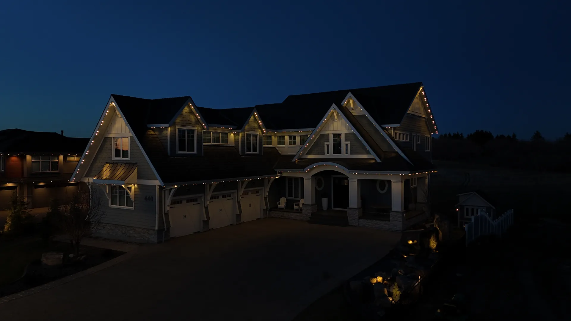 Home with warm white permanent lights along every roofline at dusk