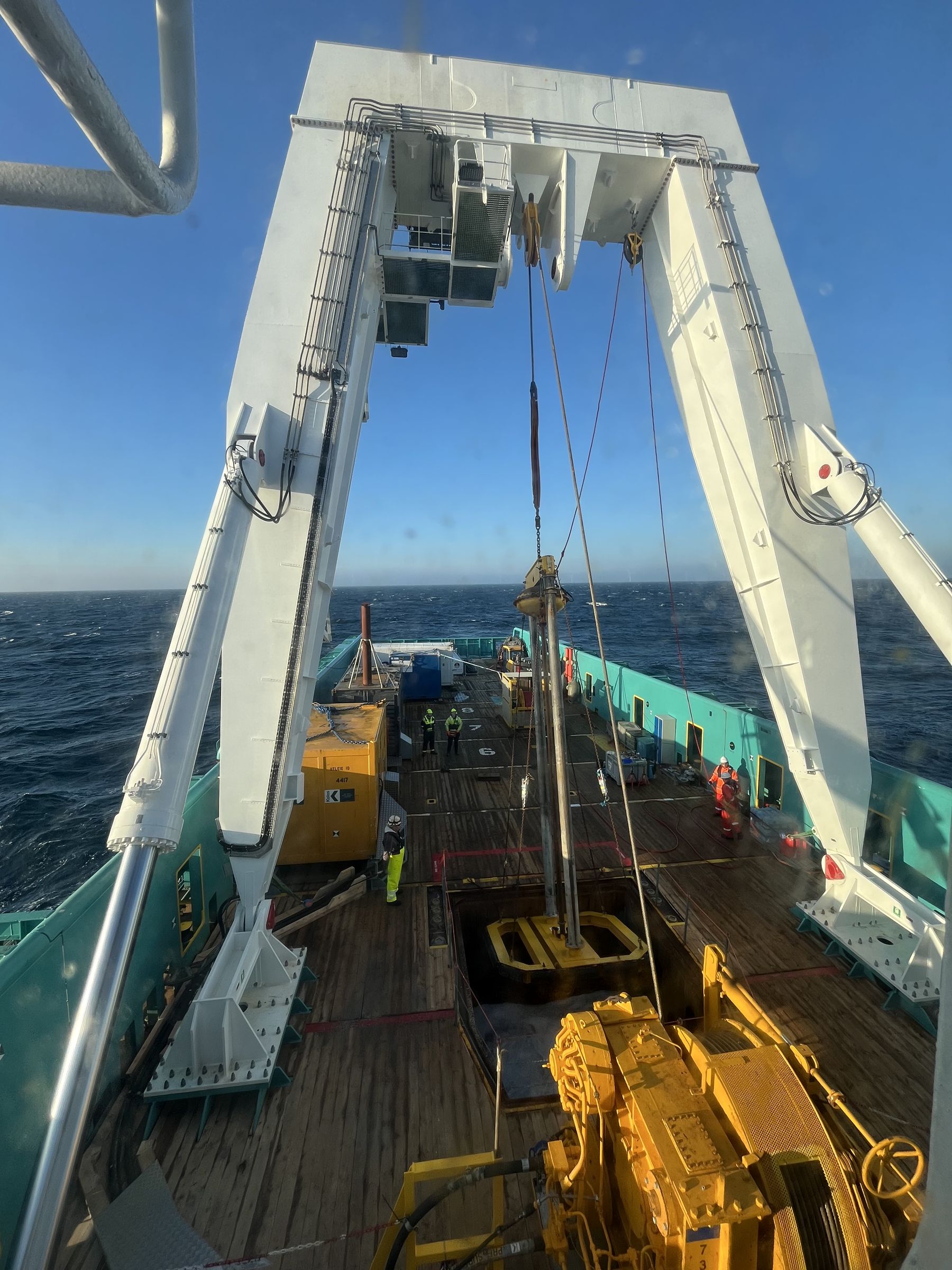 View from the bridge over Ross Eagle's aft deck at sea, with the white A-frame above the moonpool, a yellow winch and crew working on deck