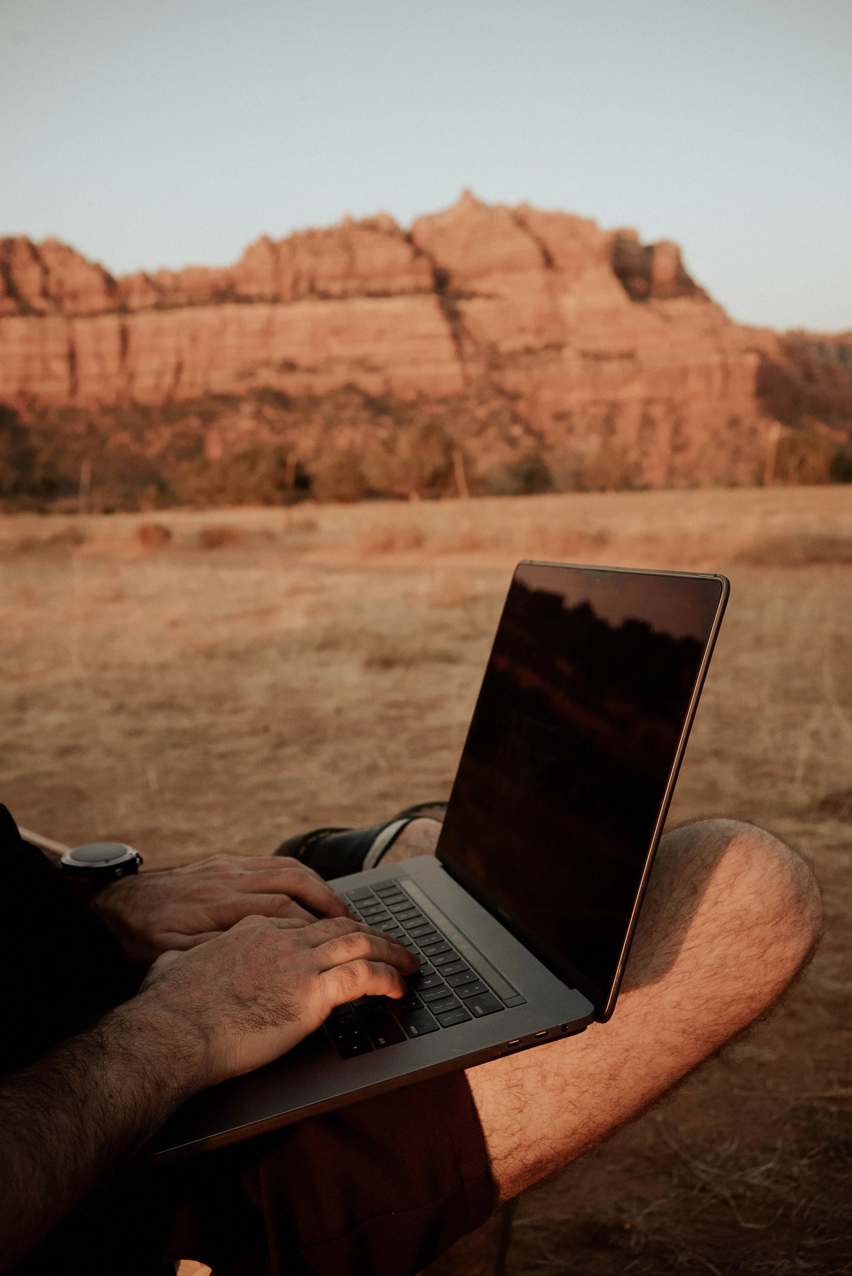 Iemand werkt op een laptop met uitzicht op rode rotsen