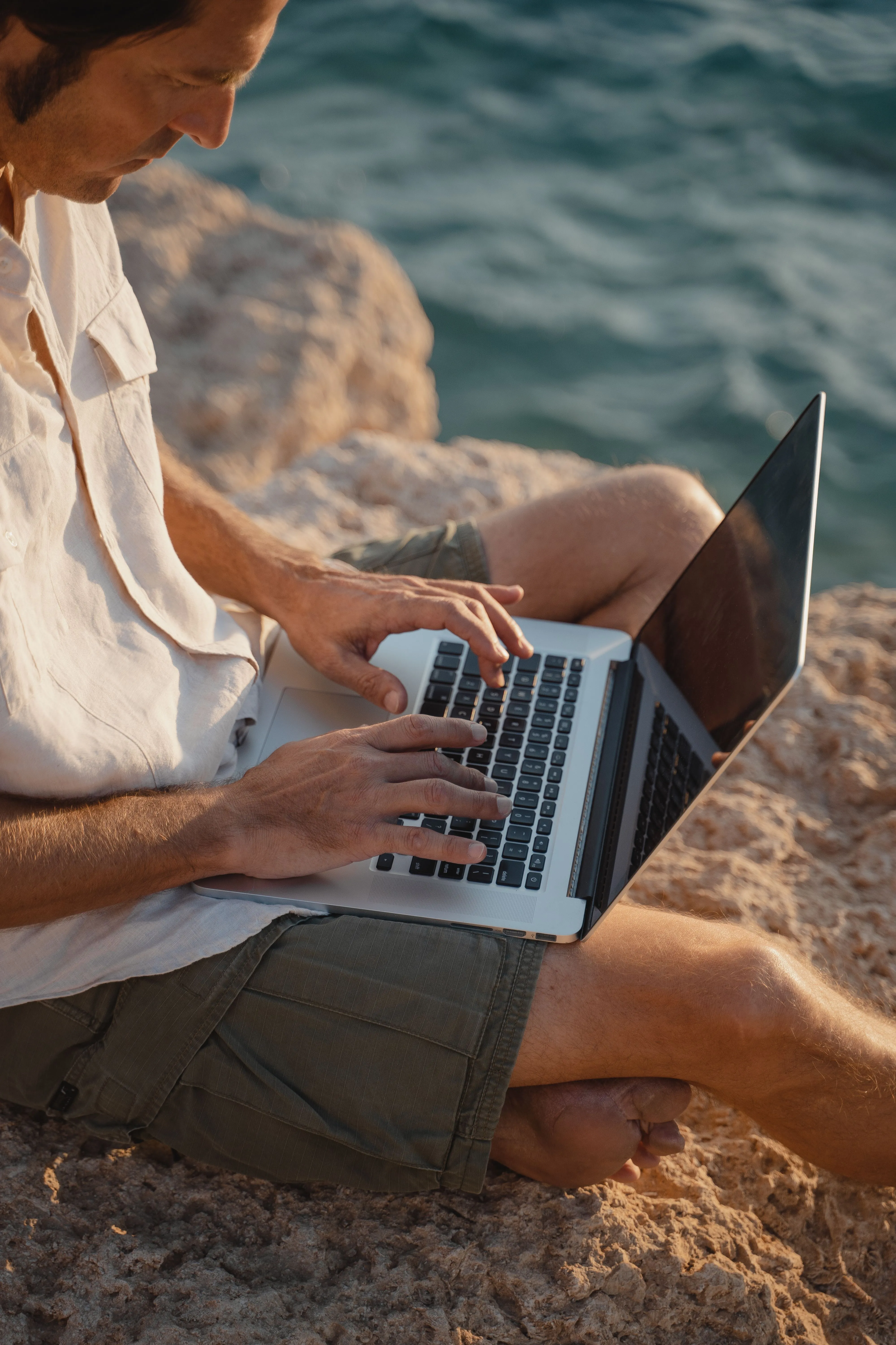 Iemand werkt op een laptop op een rots aan zee