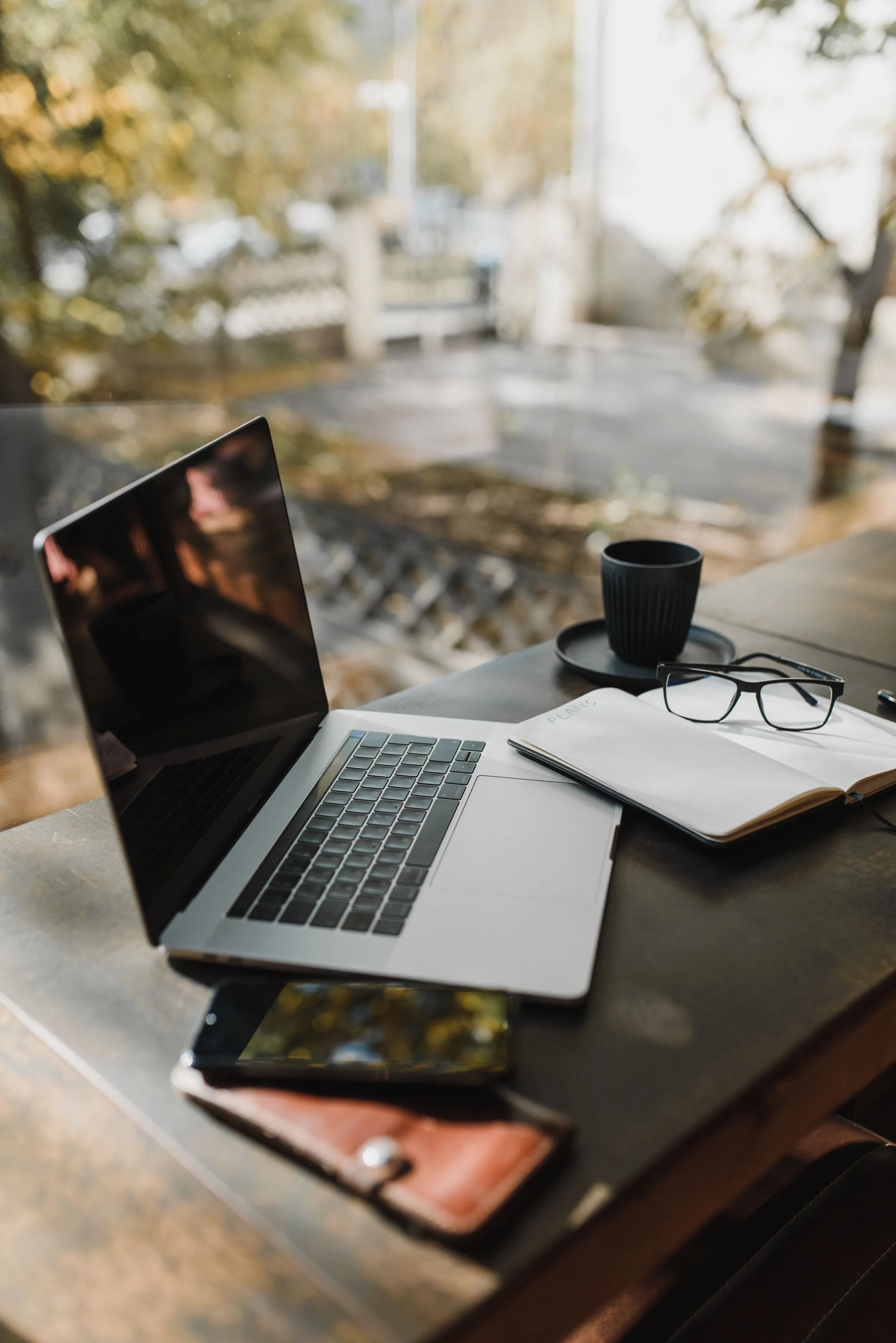 Laptop, notitieboek en koffie op een tafel bij het raam